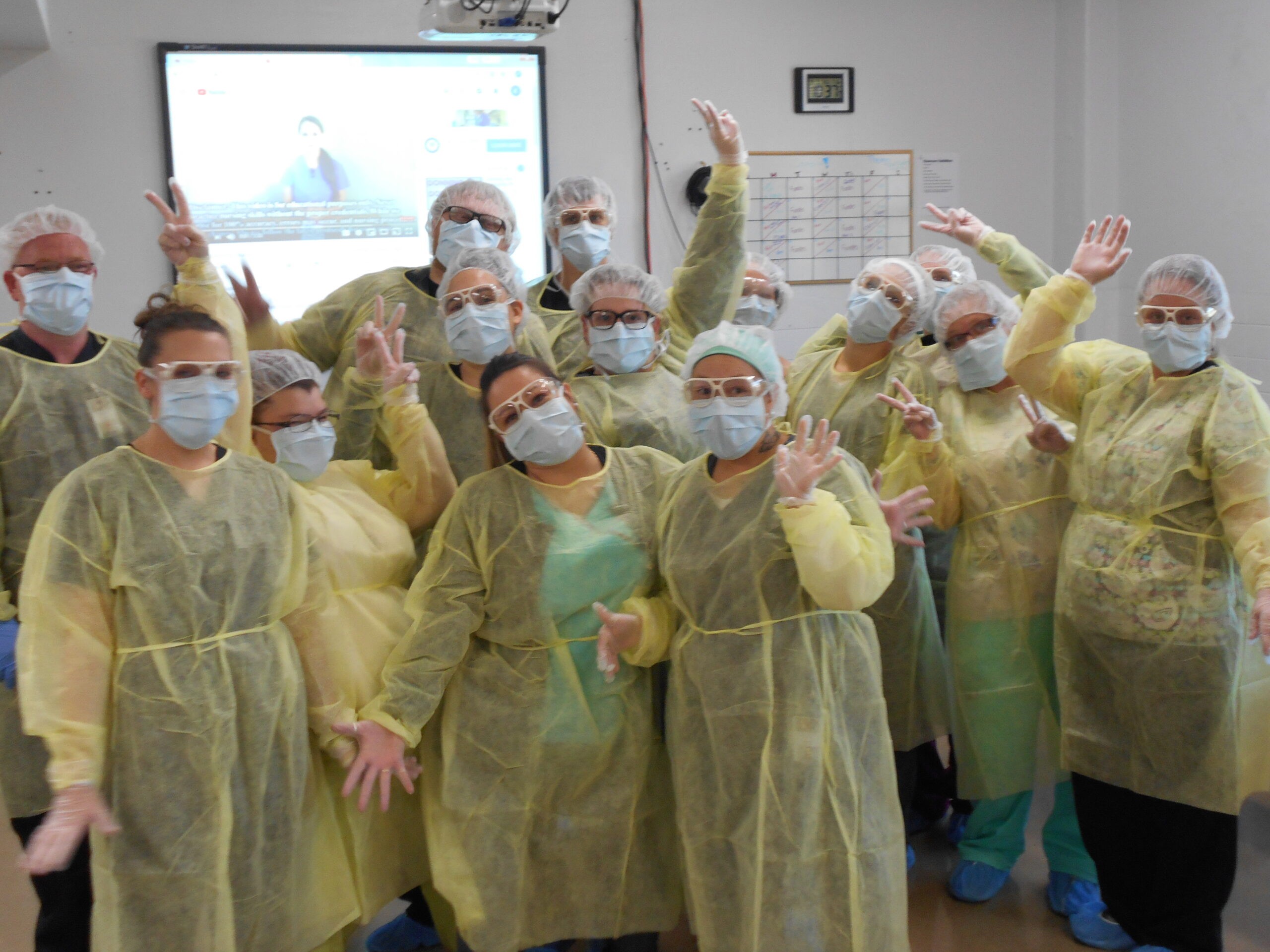 photo contains fourteen practical nursing students in yellow disposable gowns, masked and happy to be in their second semester.
