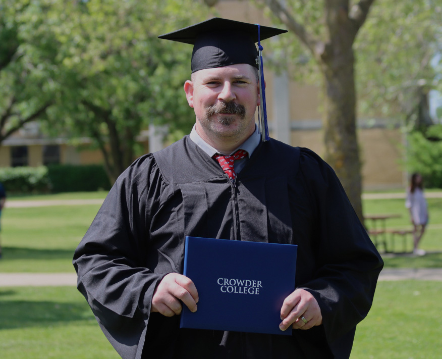 Graduate with degree , cap, and gown standing on campus lawn