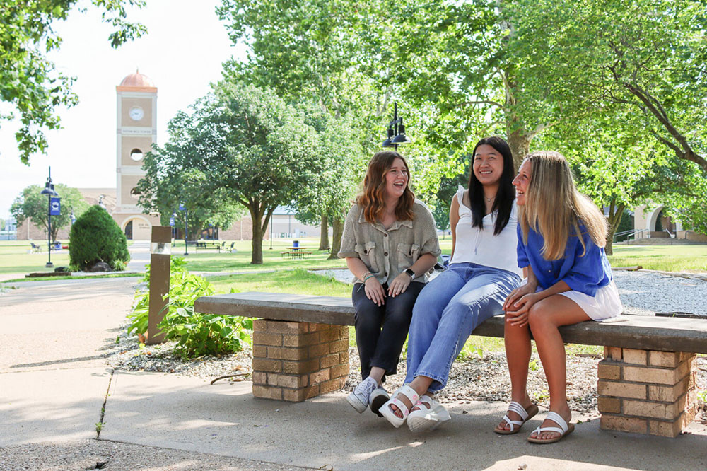 Students laughing together outside on a campus bench
